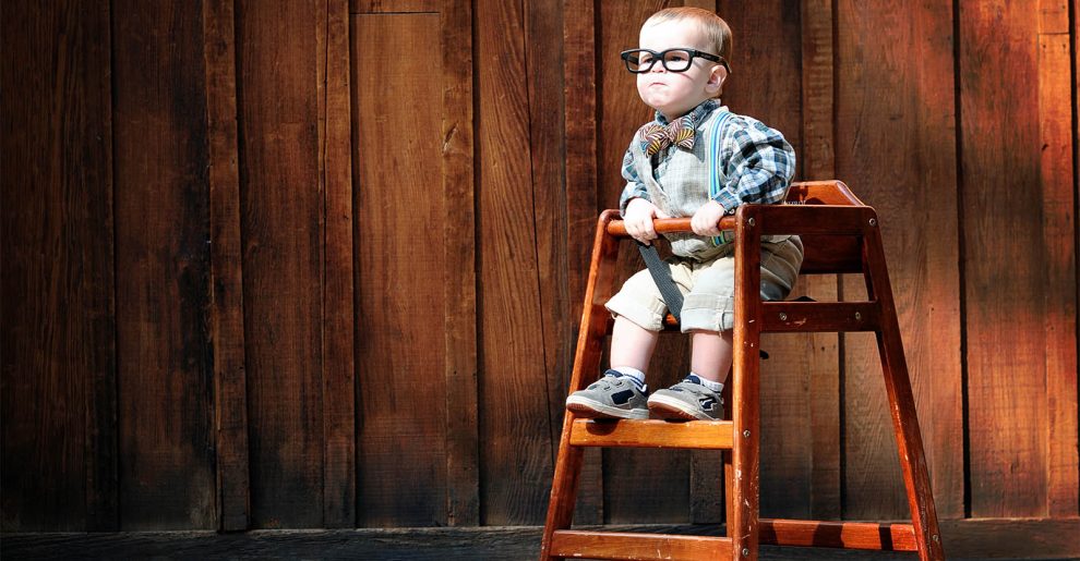 mały filozofi siedzi na wysokim krzesełku na tle drewnianej ściany